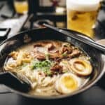 Close-up of a creamy Hokkaido ramen bowl with ground pork, peanuts, chili oil, a soft-boiled egg, and green onions. This spicy, rich version offers bold flavor and texture with a nutty twist.