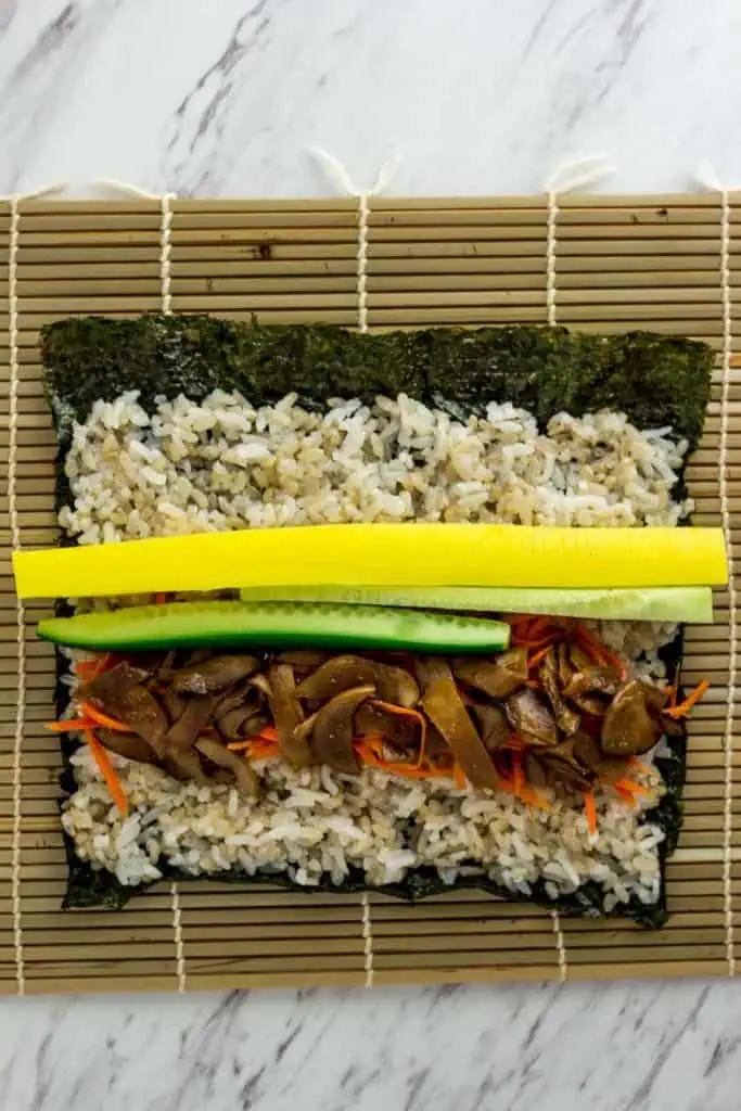 Bulgogi mushrooms, carrots, cucumber, and pickled radish layered on rice before rolling vegan kimbap