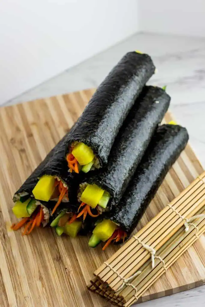 Whole vegan kimbap rolls filled with bulgogi mushrooms and vegetables on a cutting board