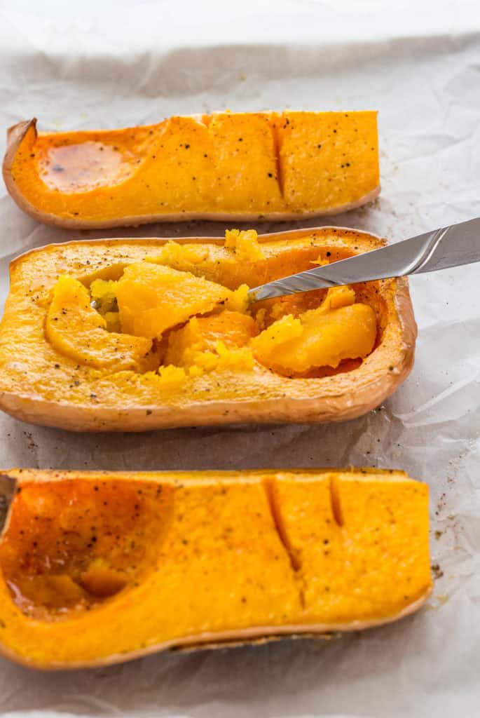 Roasted butternut squash with golden flesh being scooped out after baking until tender.