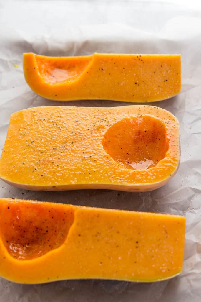 Fresh butternut squash halves brushed with olive oil, ready to roast for vegan butternut squash soup.
