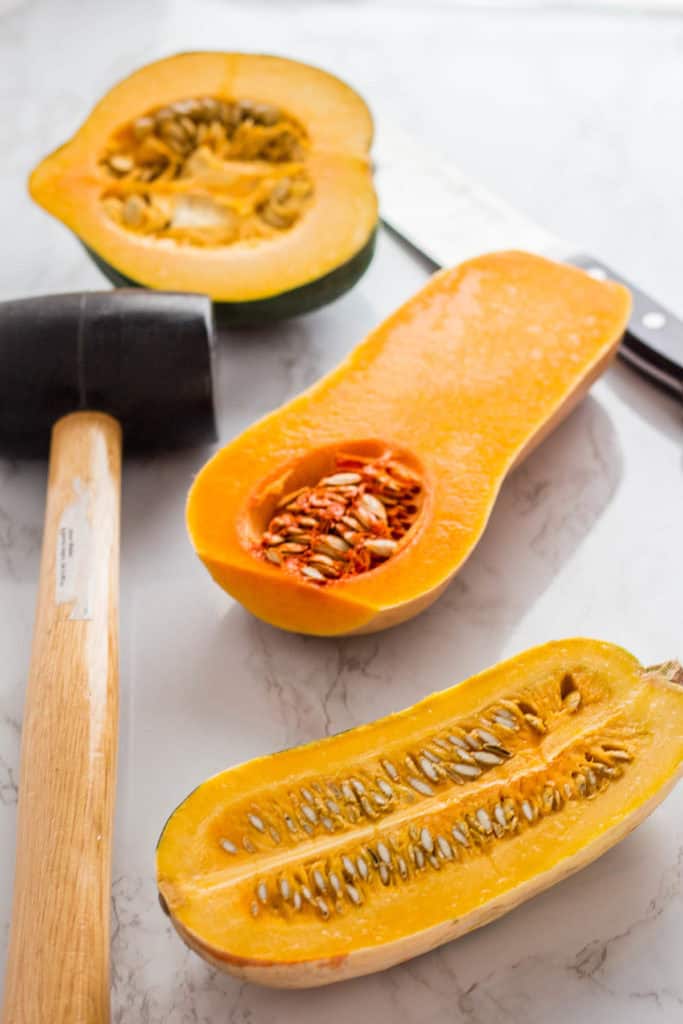 Halves of acorn squash, butternut squash, and delicata squash with rubber mallet and knife