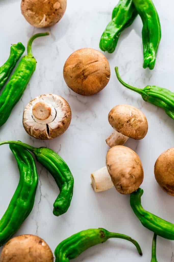 Baby bella mushroom and shishito peppers on white background marvel surface