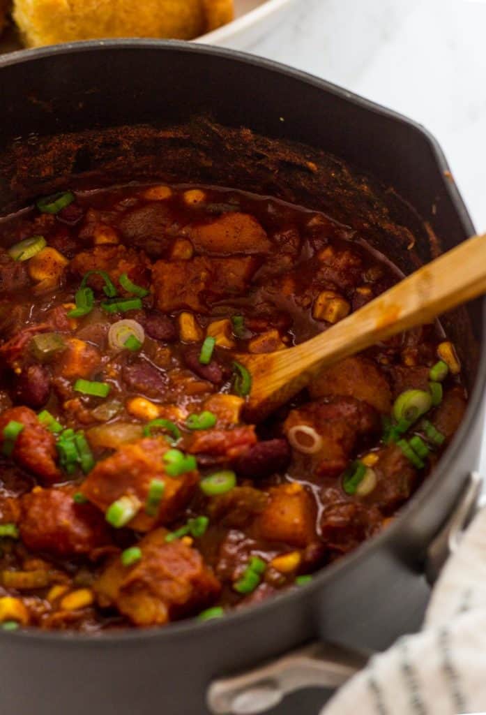 Close-up of a pot of vegan butternut squash chili with roasted squash, corn, and kidney beans stirred together.