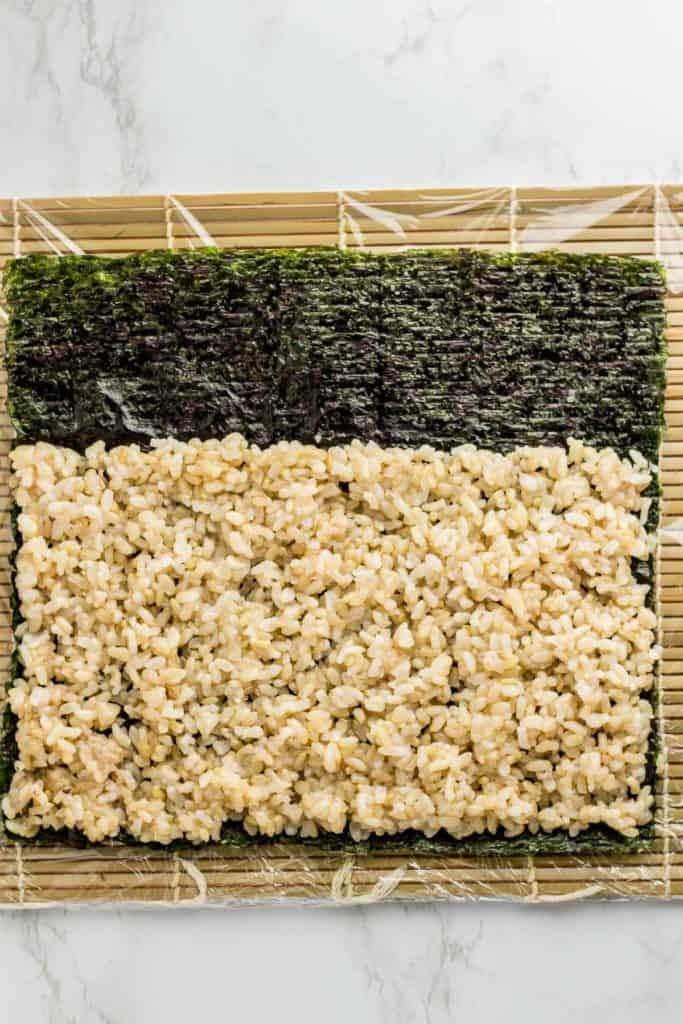 Rice is spread evenly on top of seaweed paper. Rice was not added to top part of the seaweed paper. About one third of the seaweed paper does not have rice.