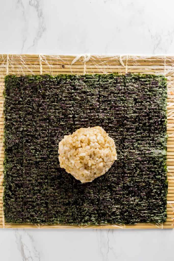 one cup of sushi rice on top of seaweed paper that is placed on top of wrapped sushi mat