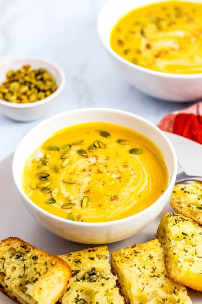 Close-up of creamy vegan butternut squash soup topped with pumpkin seeds, served with garlic bread slices.