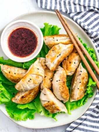 Pan-fried vegan bulgogi mandu served on lettuce with dipping sauce and chopsticks.