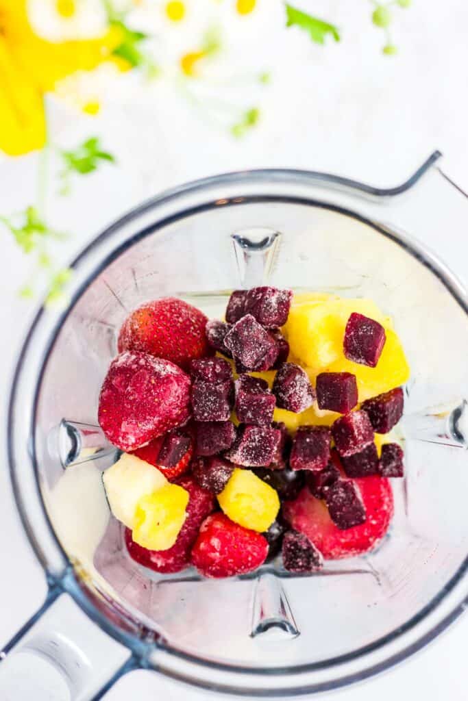 Overhead view of blender with frozen beet cubes, pineapple, and strawberries ready to blend for beetroot smoothie.