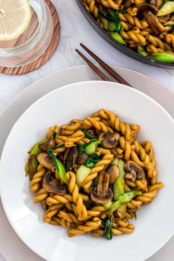 Bowl of bok choy mushroom pasta served with chopsticks on the side.