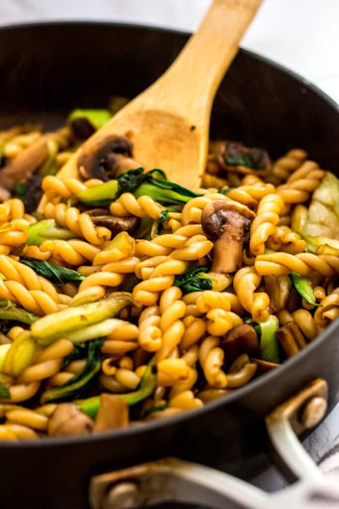 Bok choy and mushrooms mixed with pasta in a skillet for a stir fry recipe.