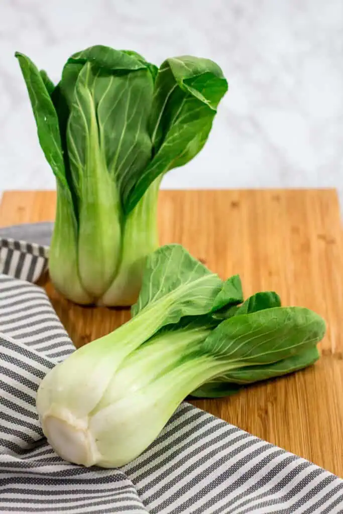 Fresh bok choy heads on a wooden cutting board, ready to be prepared.