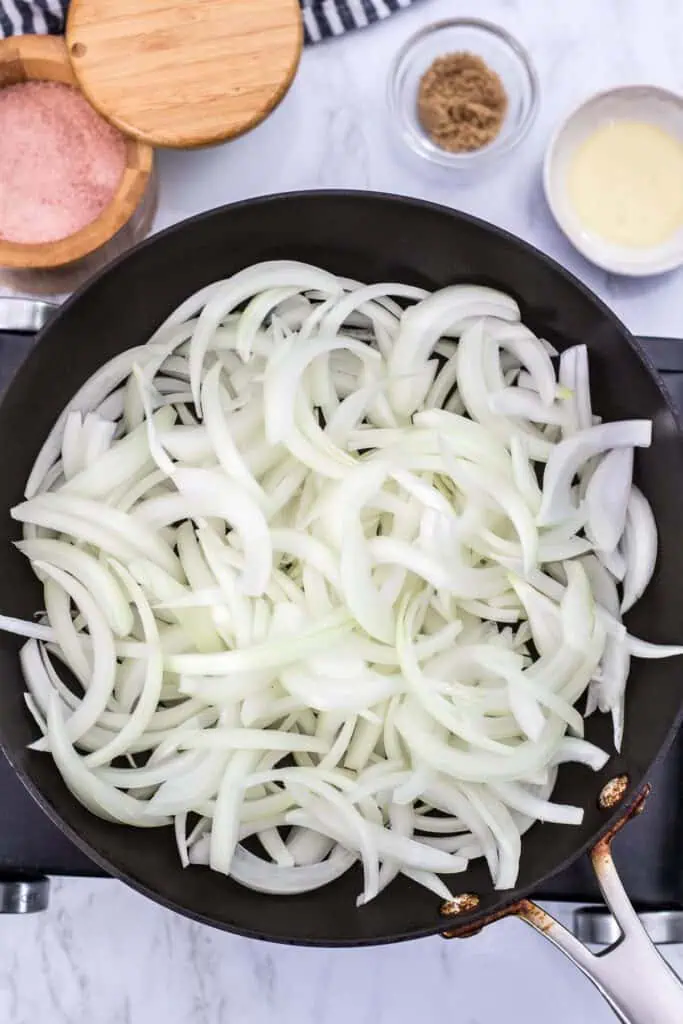 Thinly sliced onions spread in a skillet before cooking for caramelized onions