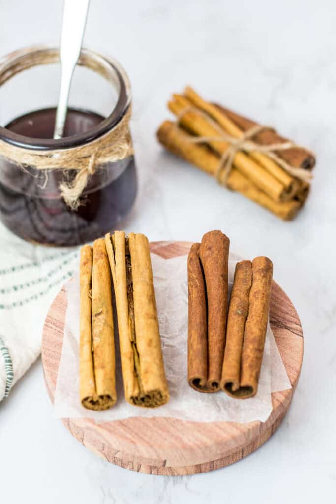 Cassia and Ceylon cinnamon sticks displayed on parchment paper next to a jar of homemade cinnamon syrup.