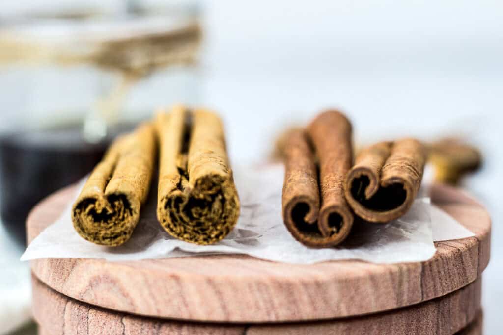 Close-up of Cassia and Ceylon cinnamon sticks on a wooden board with homemade cinnamon syrup in the background.