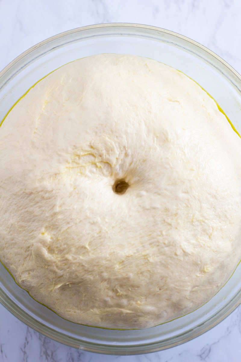 risen dough in the bowl with the indentation made with a finger tip in the middle.