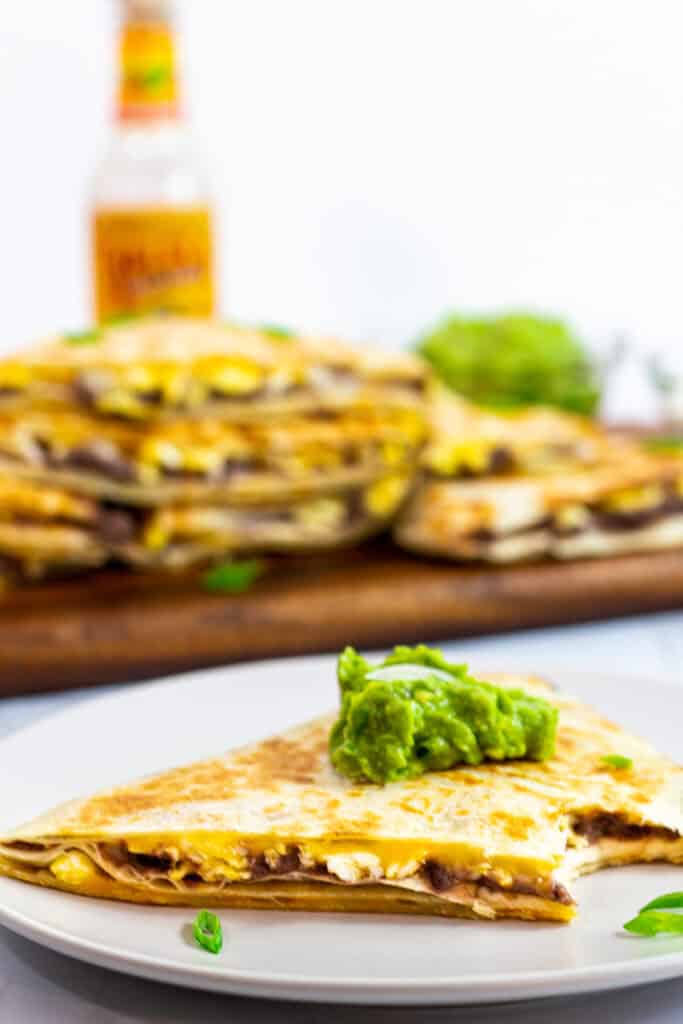 A piece of breakfast quesadilla with refried beans and eggs with a dollop of guacamole on top.