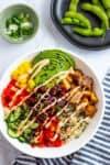 Beet poke bowl topped with avocado, tofu, vegetables, and spicy mayo drizzle