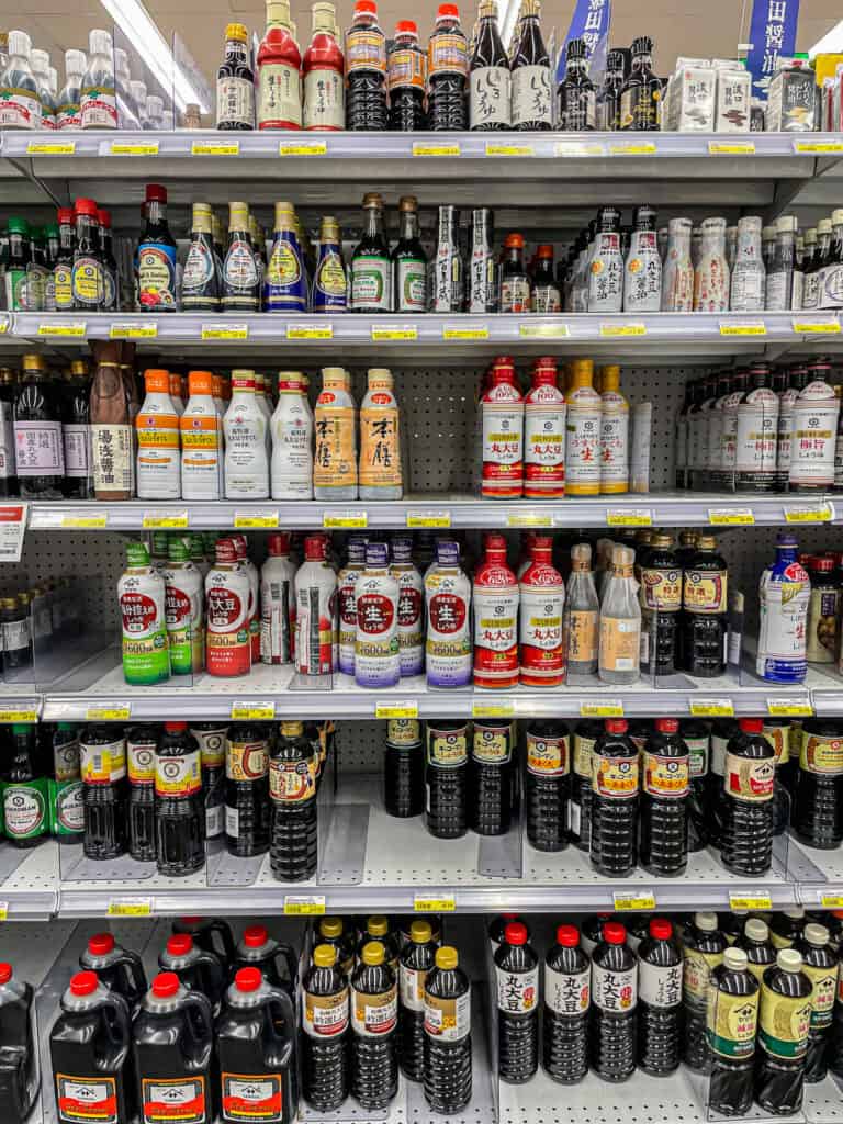 Wide variety of soy sauce bottles and Japanese cooking condiments neatly displayed on a grocery store shelf, featuring different brands and types.