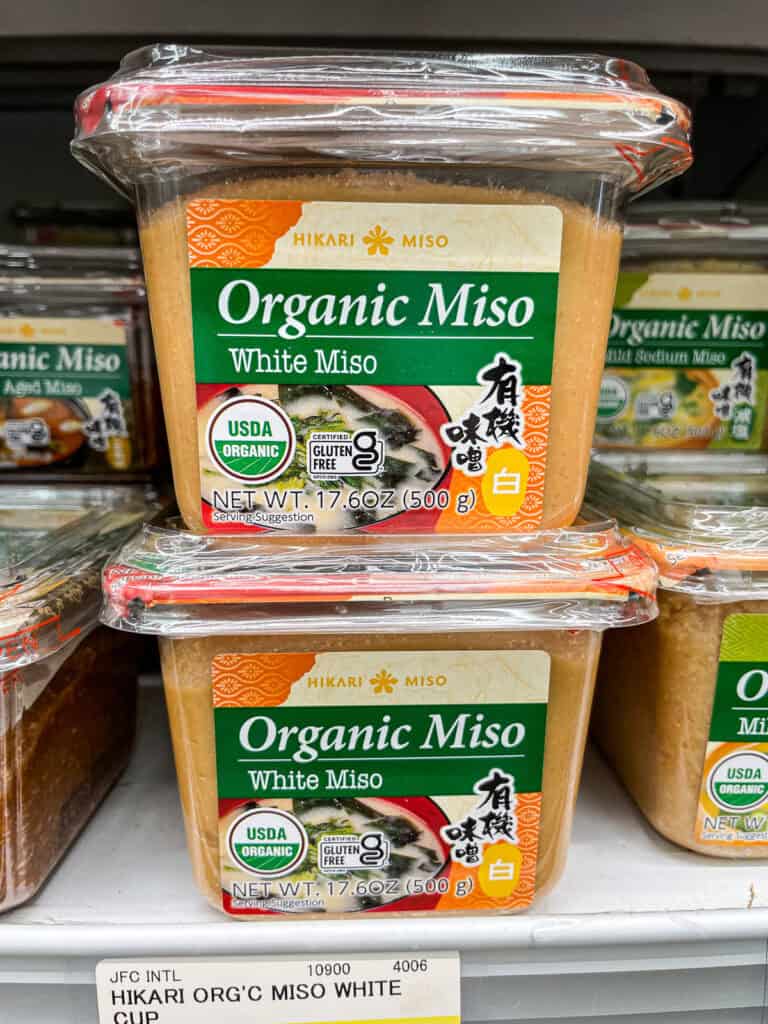Close-up of Hikari brand organic white miso tubs on a grocery shelf, a staple ingredient in Japanese cooking.