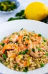 Bowl of couscous risotto with shrimp and leeks, garnished with parsley and lemon zest