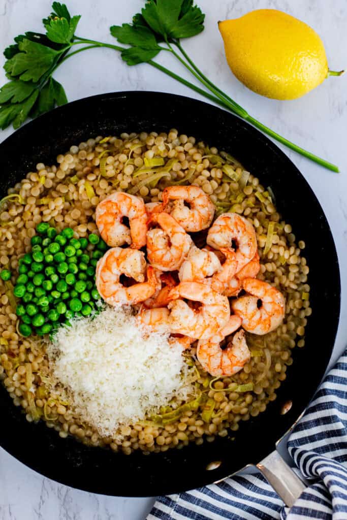 Pan of couscous risotto with shrimp, peas, and grated Parmesan ready to stir together