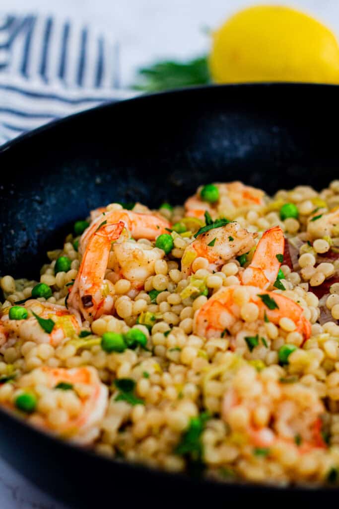 Creamy couscous risotto with shrimp, peas, and leeks in a skillet, garnished with parsley