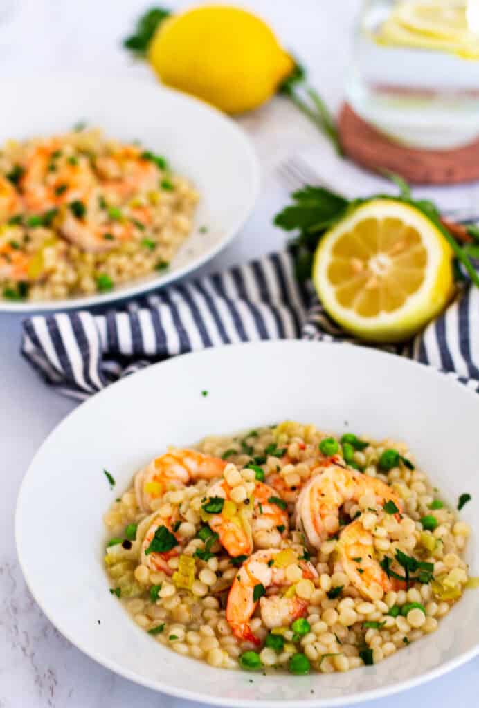 Two bowls of creamy couscous risotto with shrimp and leeks, garnished with parsley