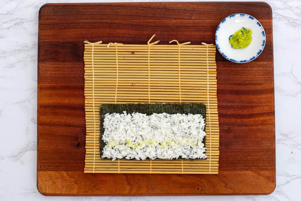 Sushi rice evenly spread on nori sheet with a line of wasabi paste, ready to roll hosomaki
