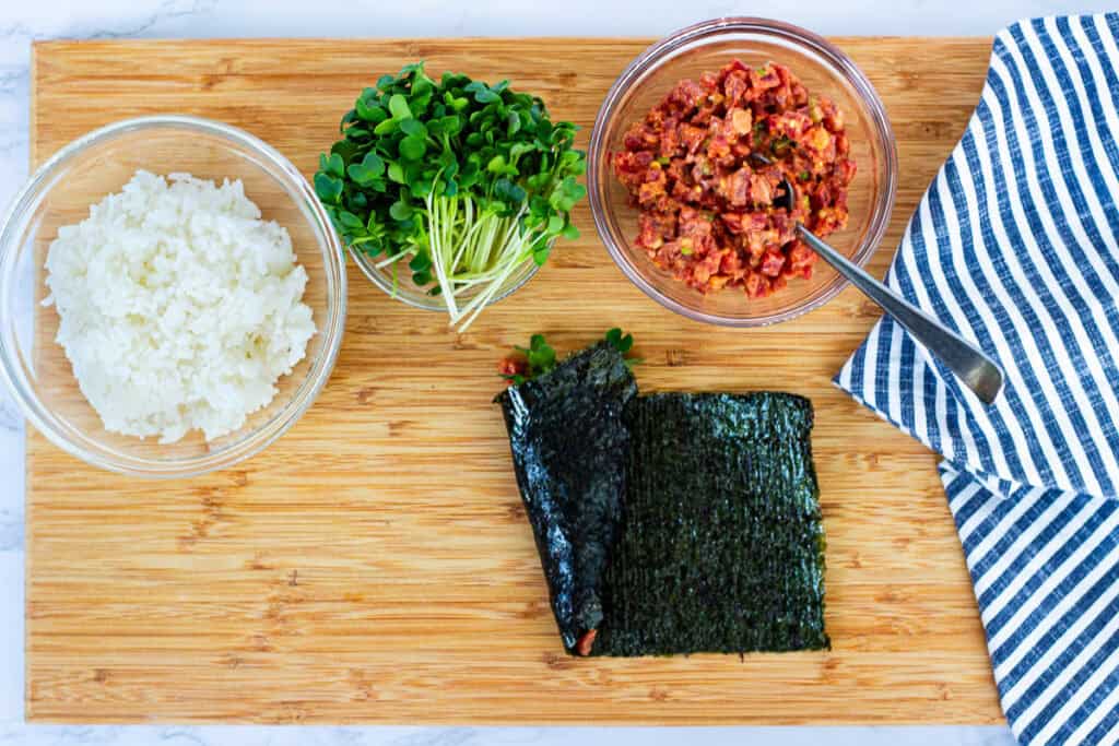 Spicy tuna hand roll fully rolled and resting on the board, with nori cone shape visible