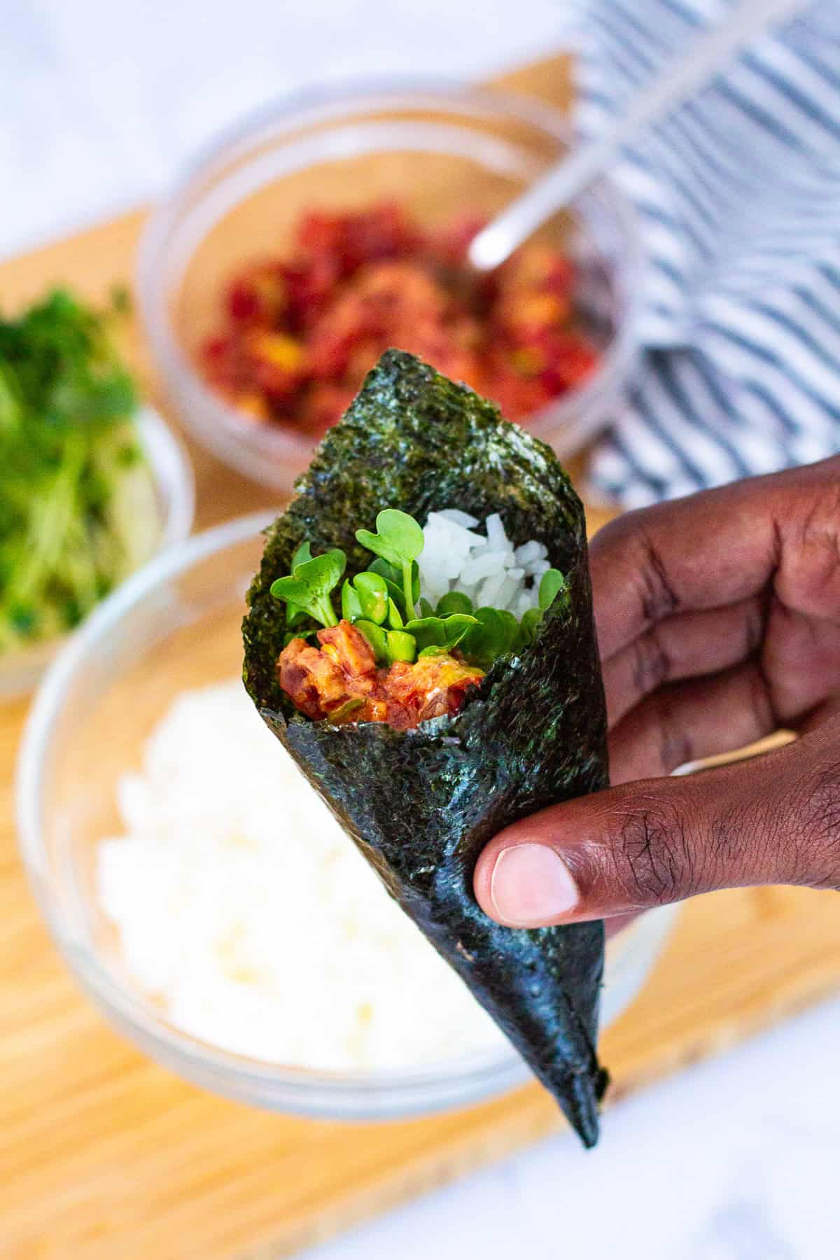 Close-up of a finished spicy tuna temaki held in hand, with rice, sprouts, and spicy tuna filling in a crisp nori cone