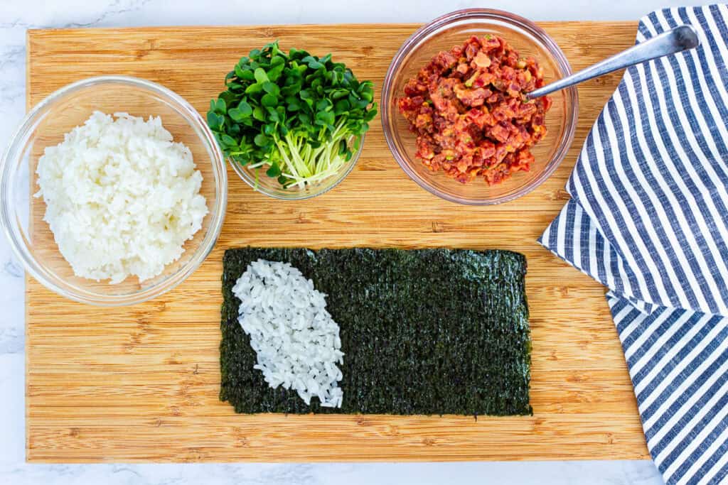 Seasoned sushi rice placed diagonally on nori sheet to start rolling a spicy tuna hand roll