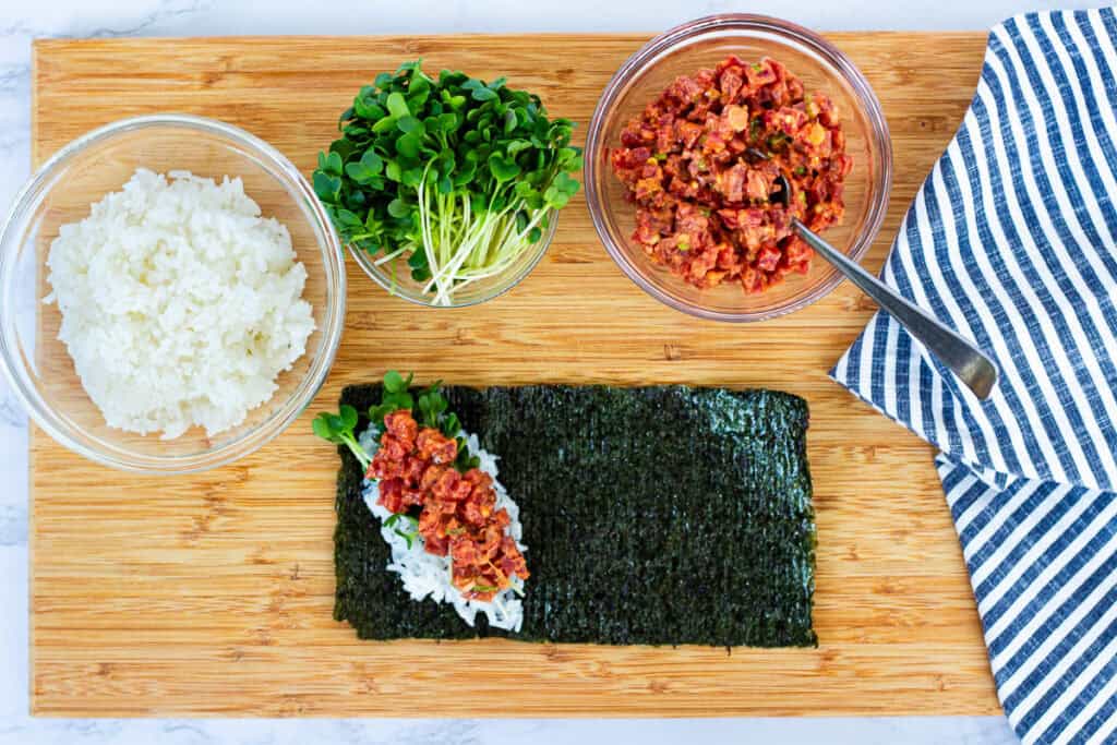 Spicy tuna and radish sprouts piled on sushi rice and nori, ready to roll a spicy tuna hand roll