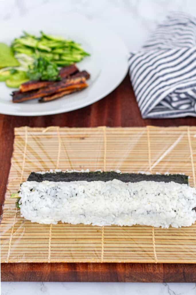 Hand-rolled unagi uramaki placed near the bamboo mat, ready to be shaped more tightly using the mat in the next step