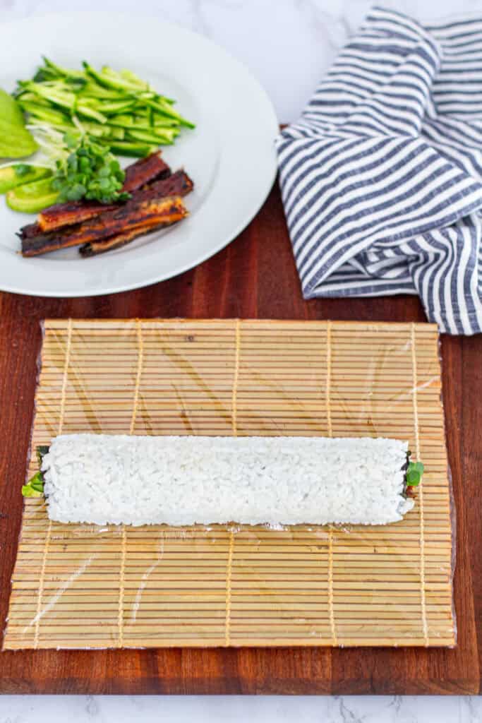 Unagi uramaki roll with rice on the outside, fully shaped and resting on a bamboo mat