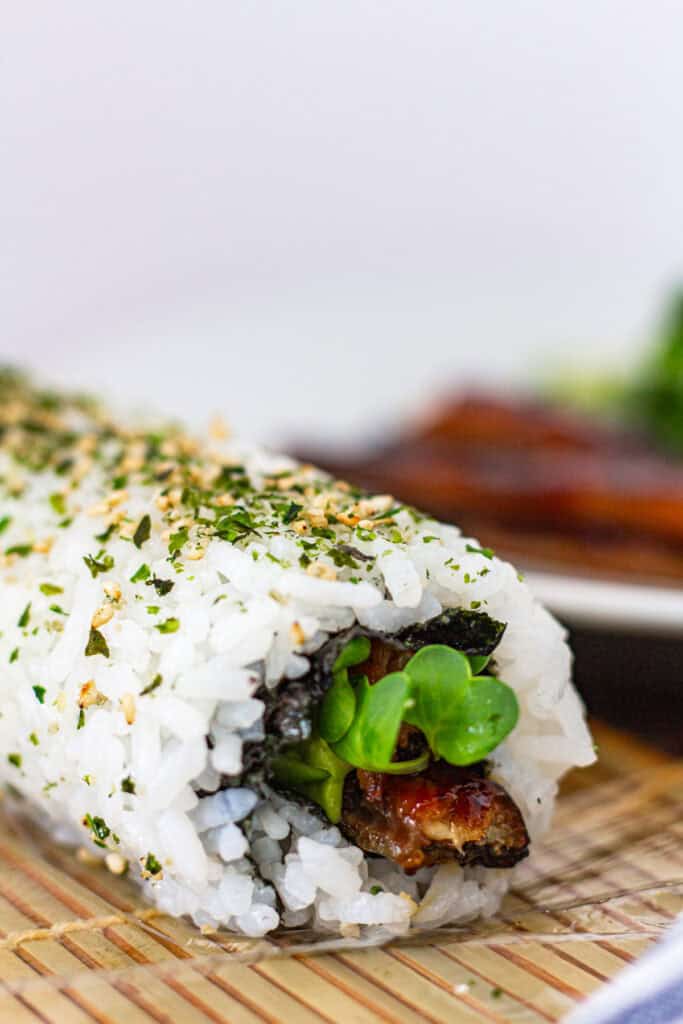 Close-up of unagi uramaki roll showing the rice coated in furikake and the filling of grilled eel and sprouts peeking out