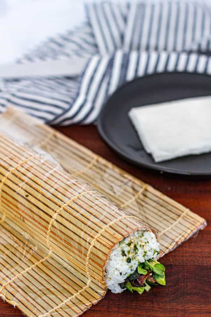 Sliced unagi uramaki roll being reshaped and tightened with a bamboo mat to neaten edges before plating