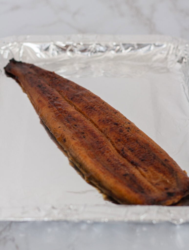 A piece of thawed grilled unagi placed on a foil-lined baking sheet before baking, ready to prepare for sushi rolls