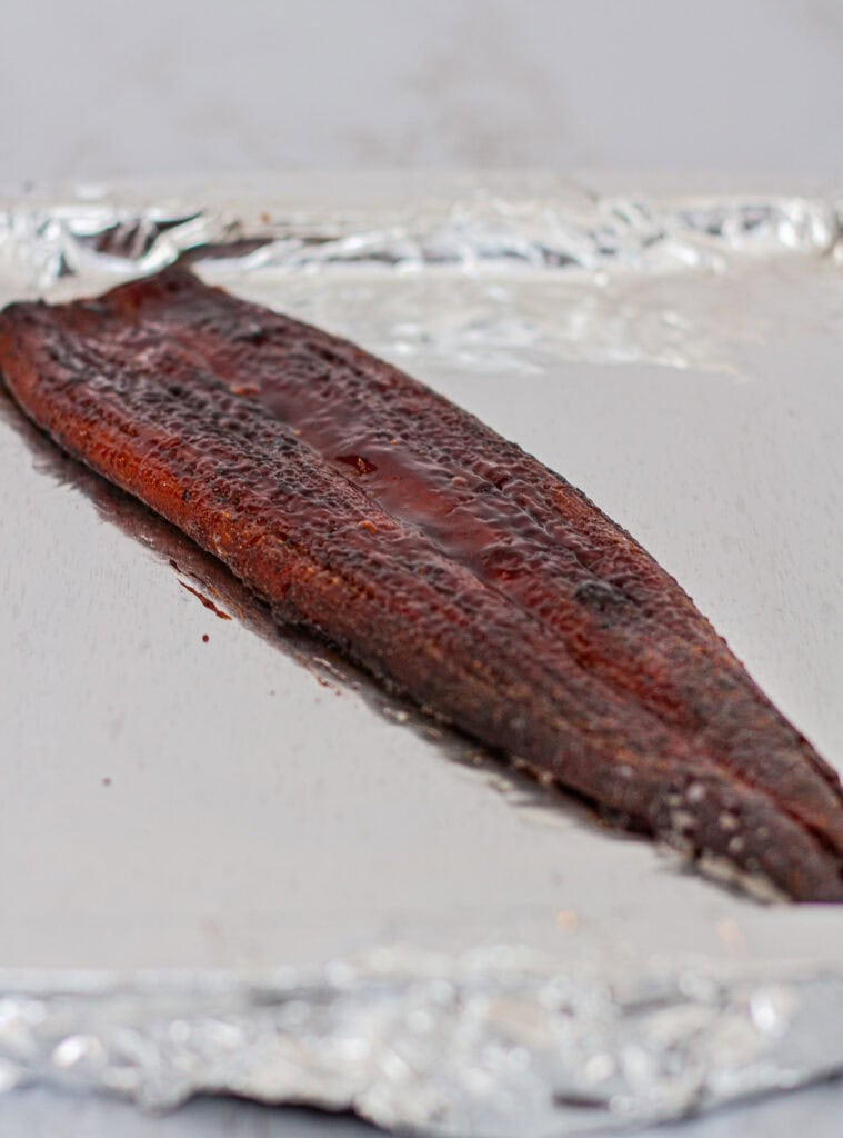 A piece of grilled unagi after baking with extra unagi sauce, glossy and ready to slice for sushi rolls