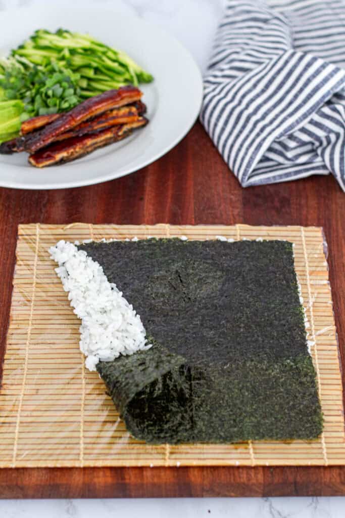 Nori sheet flipped with rice side down on a bamboo mat, showing that the bare nori edge should be closest when rolling unagi uramaki