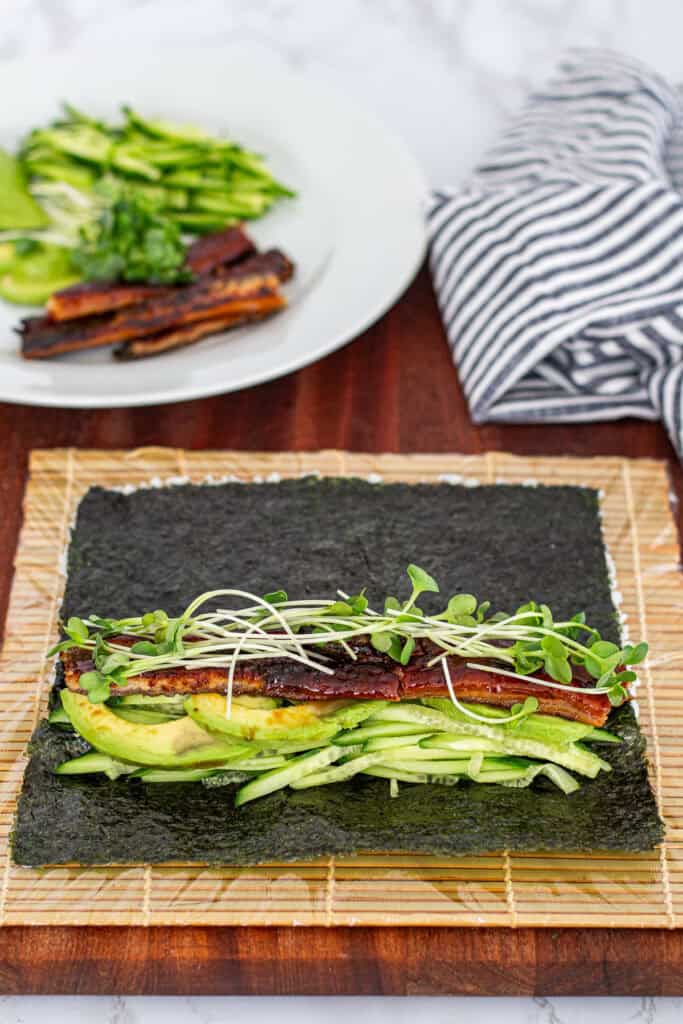 Nori sheet topped with cucumber, avocado, grilled unagi, and radish sprouts, ready to roll into an unagi uramaki sushi roll
