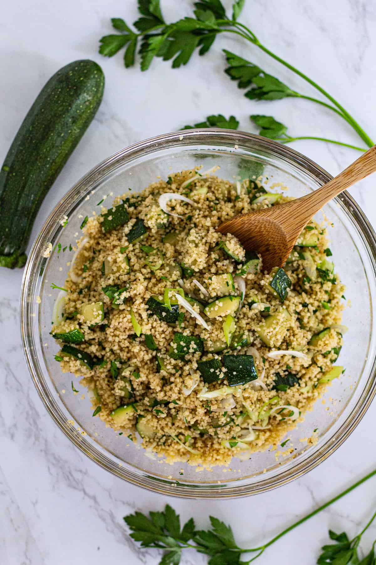 Bowl of zucchini couscous with garam masala, scallions, and parsley with a wooden spoon