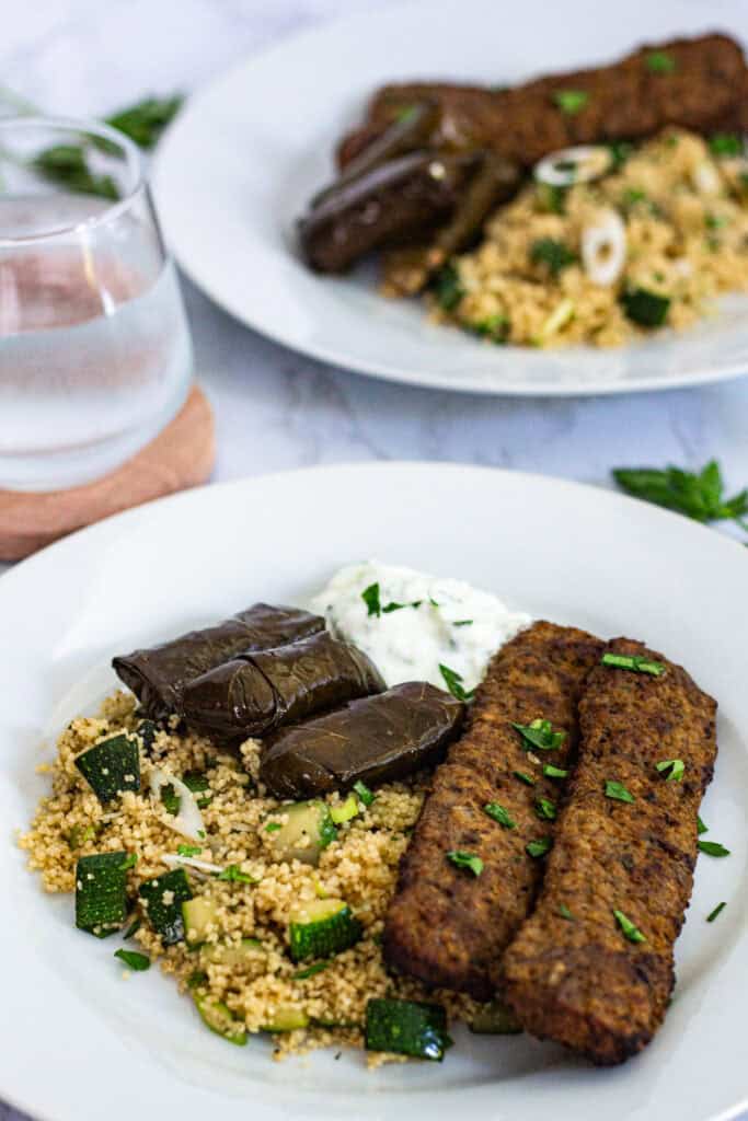 Plate of zucchini couscous with garam masala served with beef kebabs, dolmas, and tzatziki