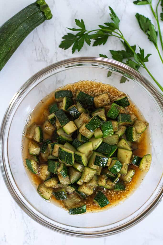Bowl of couscous topped with sautéed zucchini and hot broth before steaming for zucchini couscous with garam masala