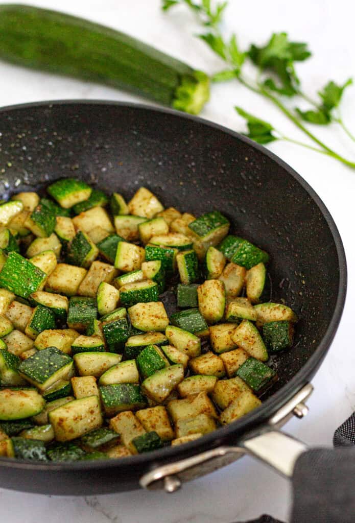 Diced zucchini sautéed with garam masala in a black skillet for zucchini couscous with Indian spices