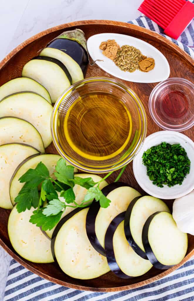 Flatlay of sliced eggplant with olive oil, parsley, garlic, and Mediterranean spices for roasted eggplant recipe