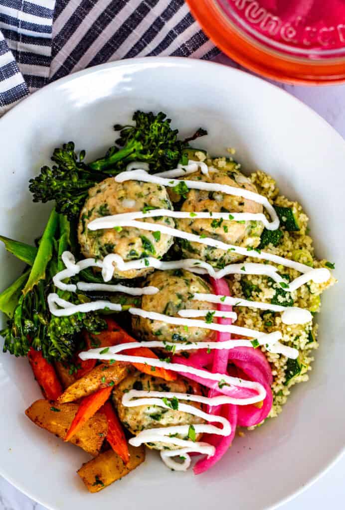 Greek chicken meatballs with zucchini couscous, roasted vegetables, and yogurt drizzle in a healthy Mediterranean bowl