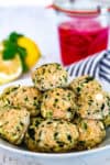 Oven baked Greek chicken meatballs with feta and herbs served in a white bowl with lemon and pickled onions in the background
