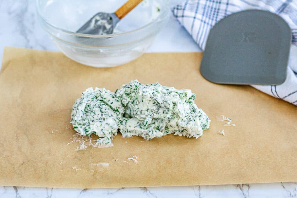 Freshly mixed herb butter shaped into a log on parchment paper, ready to be wrapped and chilled.
