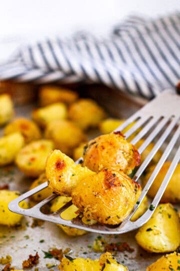 Close-up of crispy golden roasted potatoes with fresh herbs on a spatula.